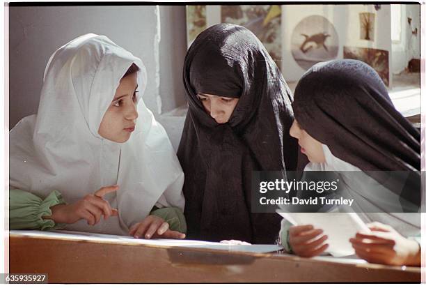 Three girls with heads covered converse at an Islamic school in central Tehran. The cooperative school is funded through government subsidies as well...