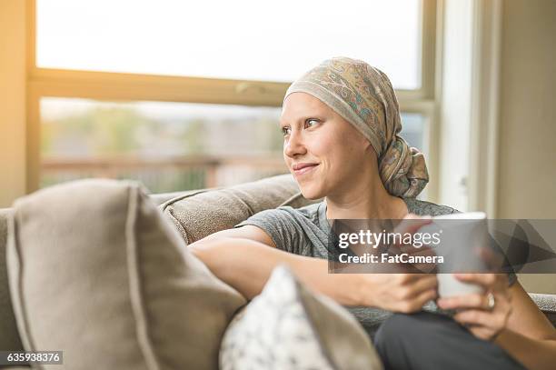 ethnic young adult female cancer patient sipping tea - bald 30s stockfoto's en -beelden