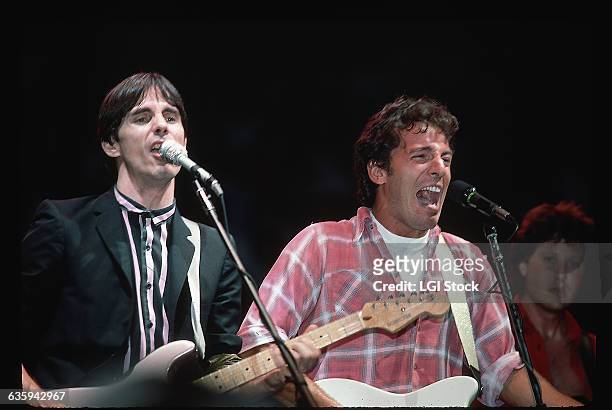 Jackson Browne and Bruce Springsteen are shown on stage, singing and playing guitar in concert.