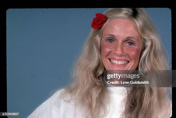 Singer/songwriter Kim Carnes is shown in a studio portrait, smiling, with a flower in her hair.