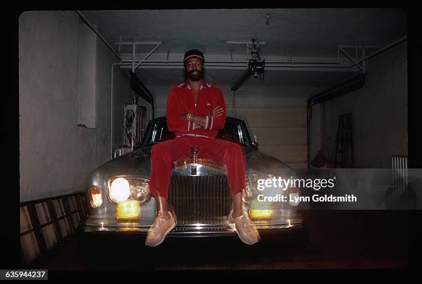 Picture shows soul singer, Teddy Pendergrass, seated on the hood of a Rolls royce and wearing a red velour sport-suit.