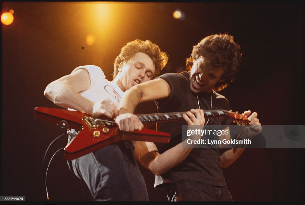 John Cougar Mellencamp Adjusting Whammy Bar on Guitarist's Electric Guitar during Performance