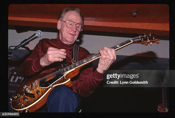 Picture shows legendary guitarist and performer, Les Paul, seated and playing the guitar .