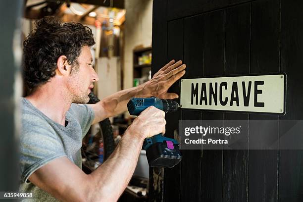 mature man fixing mancave sign on wooden door - man cave stock pictures, royalty-free photos & images