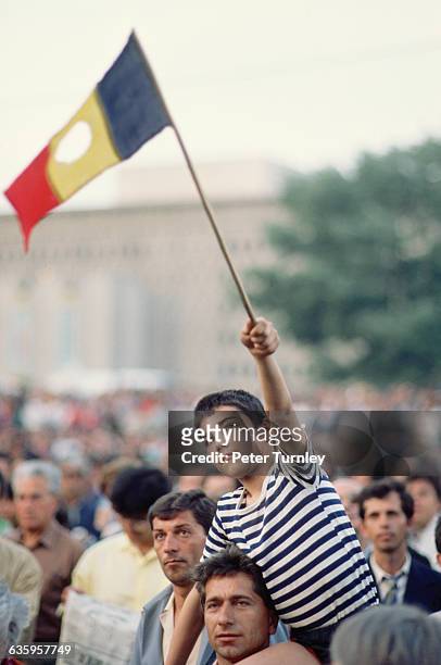 Boy on his father's shoulders waves a revolutionary Romanian flag with the Communist symbol torn out of its center at a rally opposing Ion Iliescu...