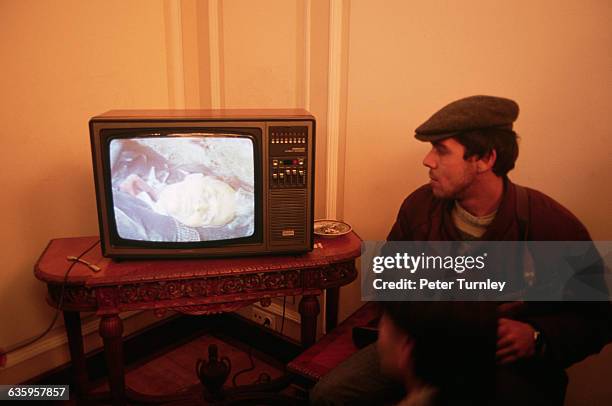 An armed rebel watches Nicolae Ceausescu's own office television set as it broadcasts photos of the dead dictator, shot by a military tribunal....