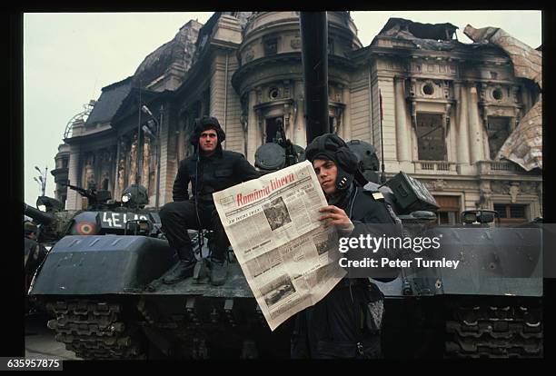 During the revolution of 1989, Romanian soldiers in Bucharest's Palace Square read a newspaper whose headline proclaims "Romania is Free" in red type.