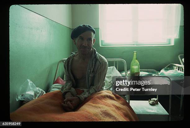 Man sits on his bed in a crowded, impoverished old age home in Bucharest.