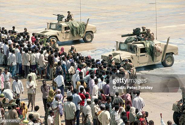 Somalis watch US soldiers in their multipurpose vehicles in position at a Mogadishu airport. In the 1980s a civil war erupted in Somalia when warlord...