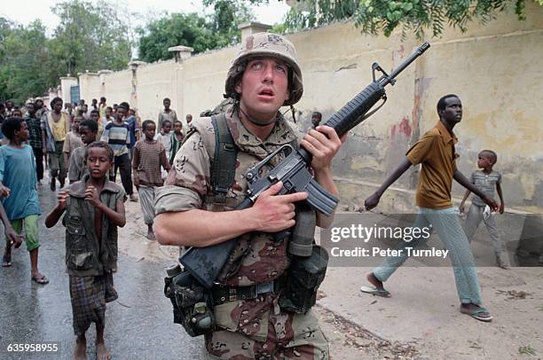 Curious locals follow an American soldier as he patrols near a building along the Green Line, which was a heavily contested area during the civil...