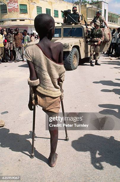 One-legged boy stands with his crutches and watches American soldiers patrol along the Green Line, which was a heavily contested area during the...