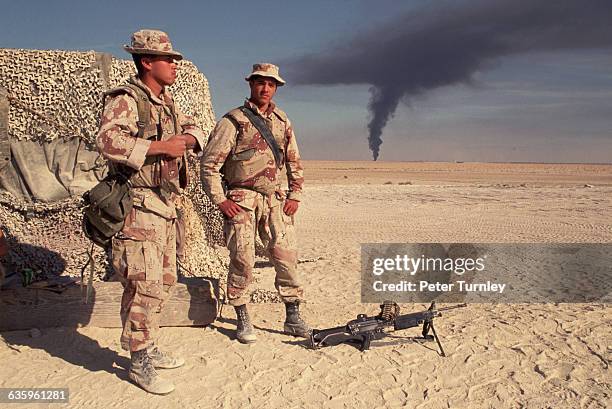 Two US Marines of the Third Battalion watch black smoke from an oil fire ascend from the horizon. As Iraq's forces retreated from Kuwait, Saddam...