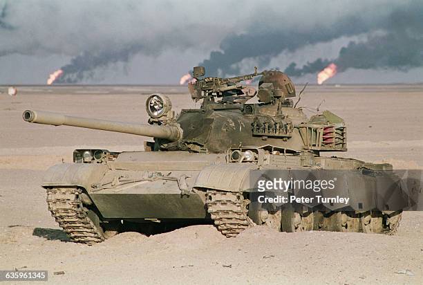 Soviet-built Iraqi T-55 tank sits in the desert at the end of the Gulf War. Oil wells burn in the background.