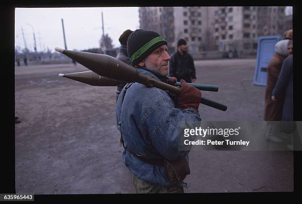 Chechen guerrilla carries missiles for bazookas over to a van.