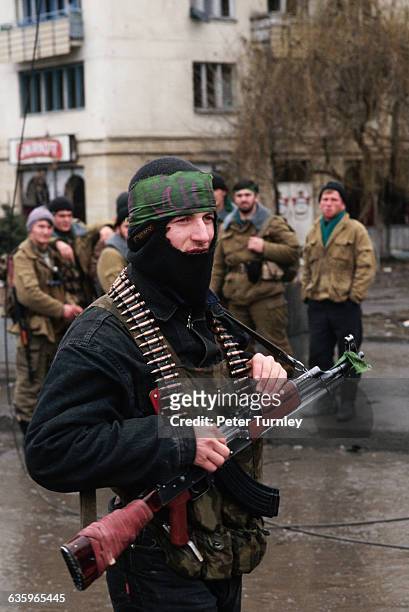 Chechen freedom fighter stands on a street in front of his guerrilla companions.