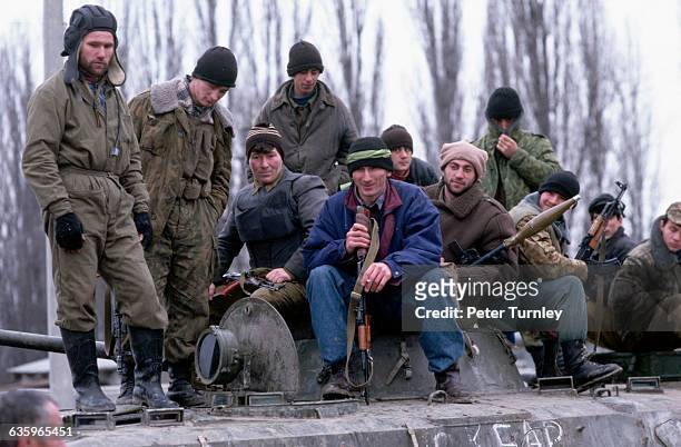 Group of Chechen guerrillas stand and sit on top of a tank.