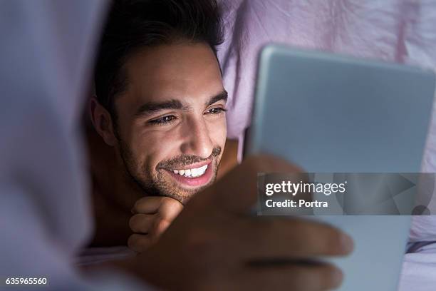 smiling man using tablet computer under blanket - under value stock pictures, royalty-free photos & images