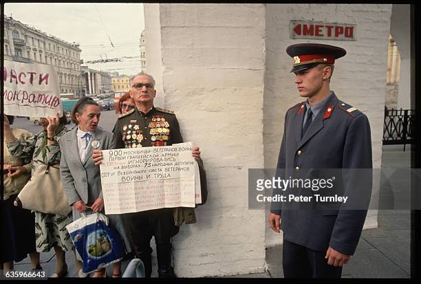 Soldier stands guard next to demonstrators holding up signs during a protest in Moscow following the Soviet Coup attempt and before the Collapse of...