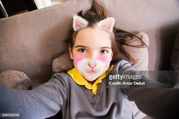 little girl using smartphone application changing her face with kitten face. - belichting stockfoto's en -beelden