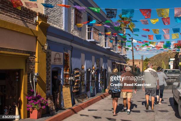 tourists walk along a flag draped street in todos santos, mexico. - baixa califórnia do sul imagens e fotografias de stock