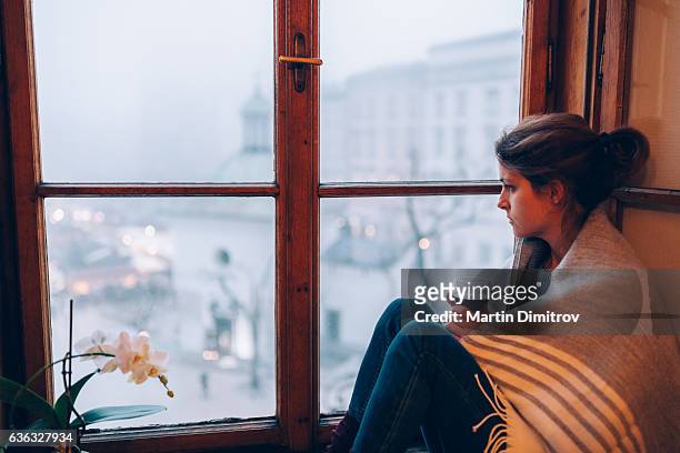 femme déprimée assise près de la fenêtre - maladie mentale photos et images de collection
