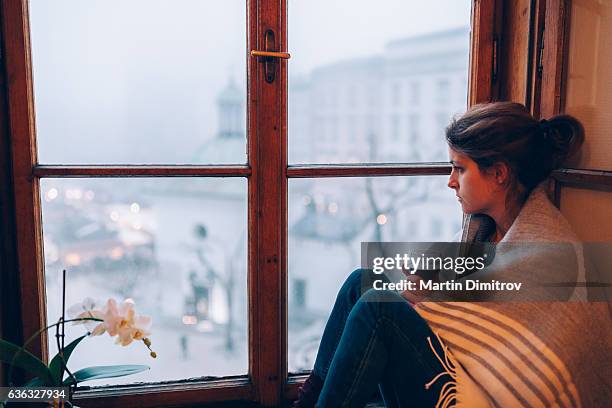 depressed woman sitting near the window - sulking stock pictures, royalty-free photos & images