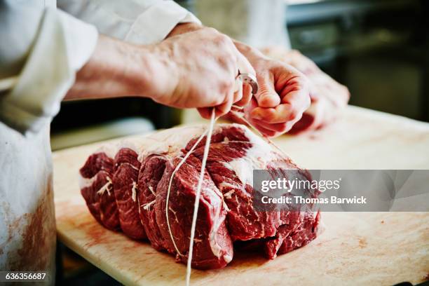 butcher tying up beef bottom round at counter - butcher stockfoto's en -beelden