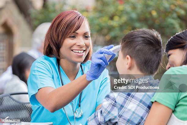 friendly nurse checks young patient's temperature at free clinic - health fair stock pictures, royalty-free photos & images