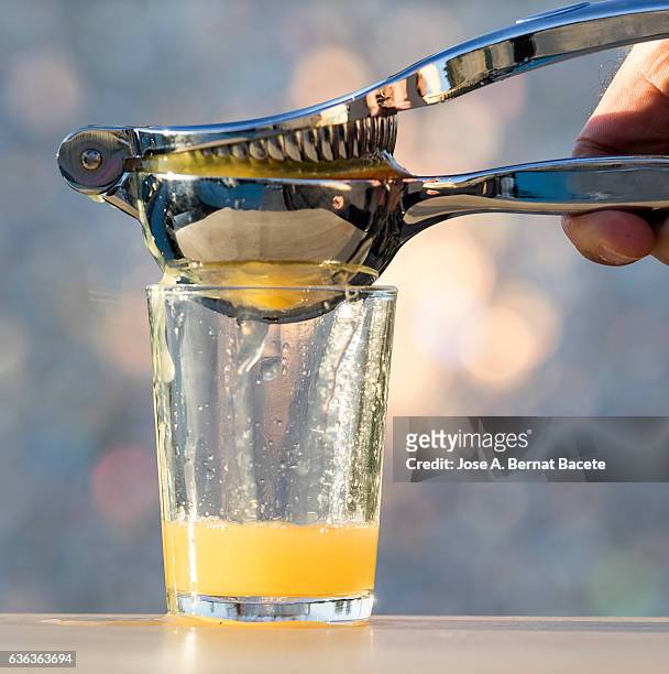 i hand from a man with a manual squeezer of oranges filling a glass of juice of orange - juice extractor stock pictures, royalty-free photos & images