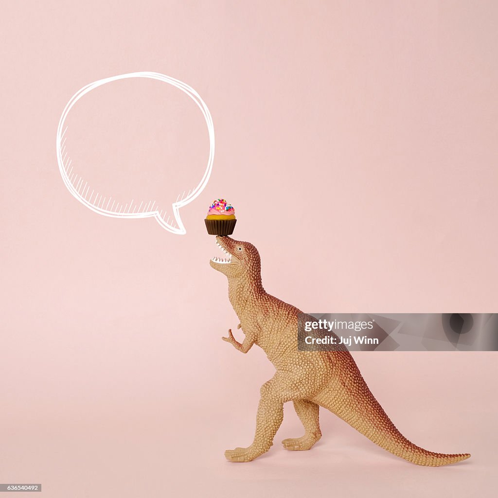 Toy dinosaur with speech bubble and cupcake