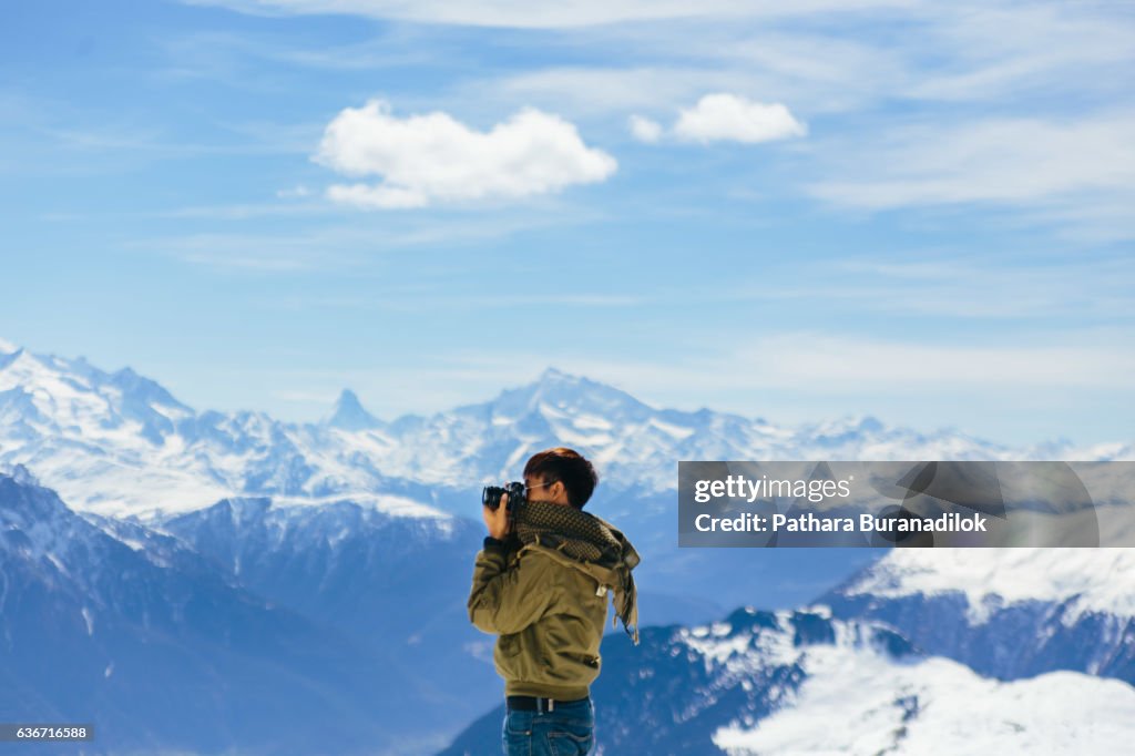 A Man taking a photo with the background of Alps