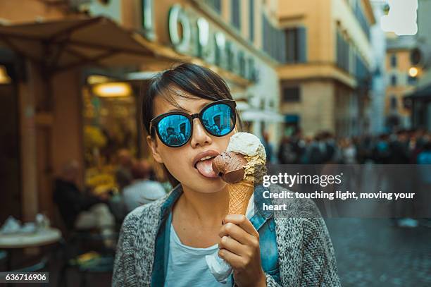 young female tourist tasting gelato / ice cream in rome street - gelato italiano fotografías e imágenes de stock