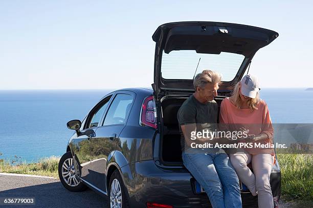couple relax on car tailgate, look at tablet, sea - couple jeans shirt stock-fotos und bilder