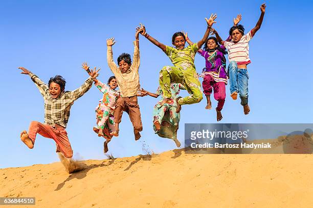 group of happy indian children jumping off dune into sand - play off stock pictures, royalty-free photos & images