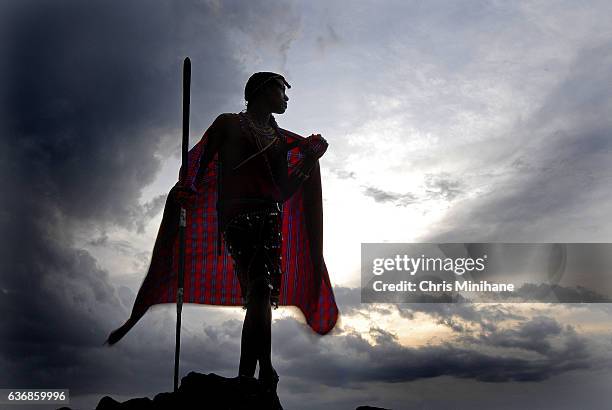 maasai warrior with back lit red blanket and dramatic sky - masai warrior stockfoto's en -beelden