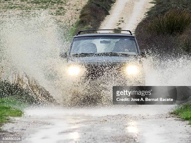 4x4 vehicle on muddy road splashing past a large puddle of rainwater, spain. - car splashing water on people stock pictures, royalty-free photos & images