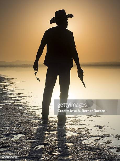 silhouette of a man with cowboy clothes and pistoala front of a lake - sheriff - fotografias e filmes do acervo