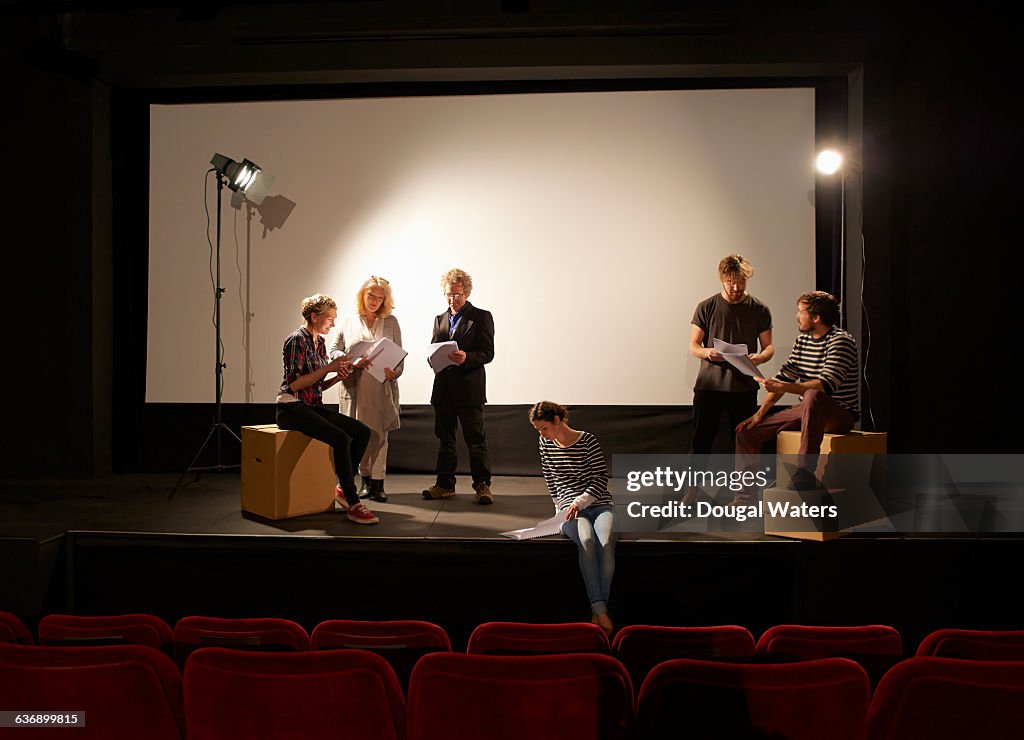 Community theatre group learning script on stage.