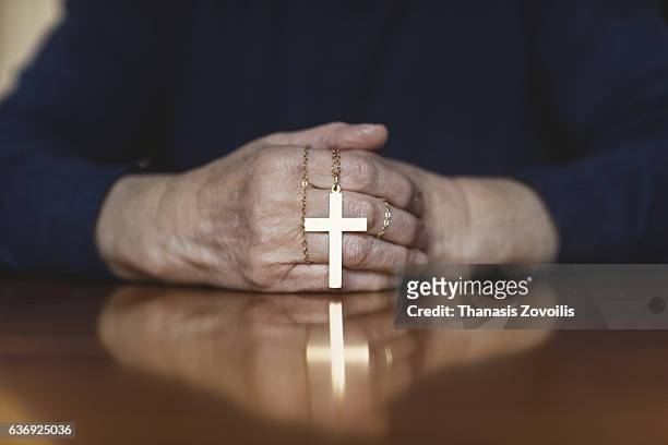 praying hands of woman with a cross on wooden desk - religion stockfoto's en -beelden