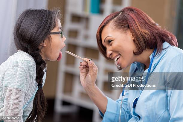 cheerful female pediatrician checks young patient's throat - girl tongue doctor stockfoto's en -beelden