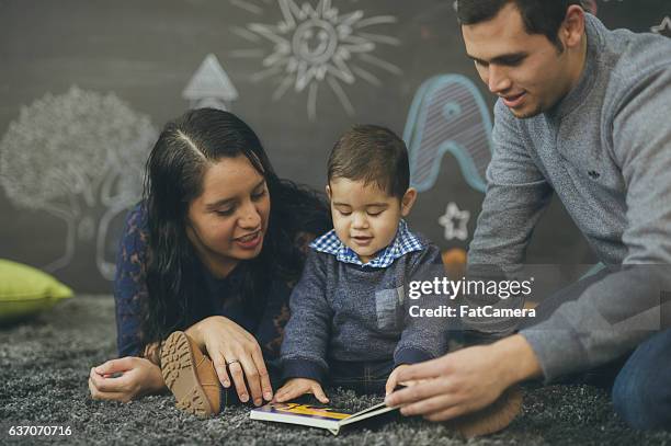 ethnic parents reading with their toddler in a playroom - draw attention stock pictures, royalty-free photos & images