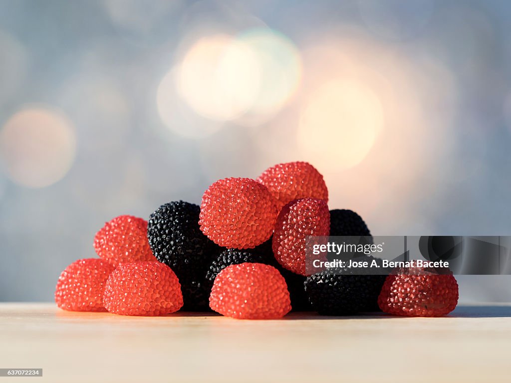 Heap of soft candies of licorice in the shape of strawberry, on a table illuminated by the light of the Sun