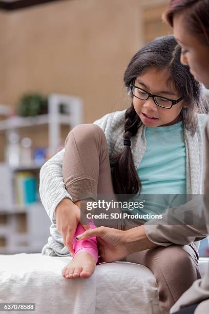 physician examines young female patient's injured ankle - distenção imagens e fotografias de stock