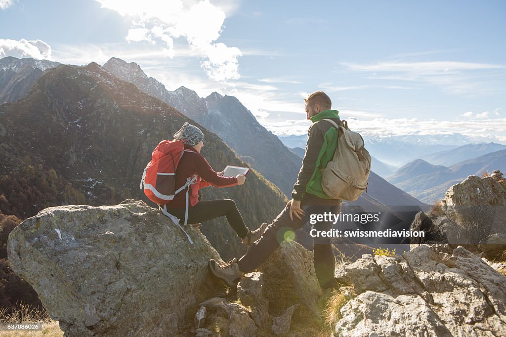 Zwei junge Wanderer auf dem Berggipfel mit Blick auf digitales Tablet