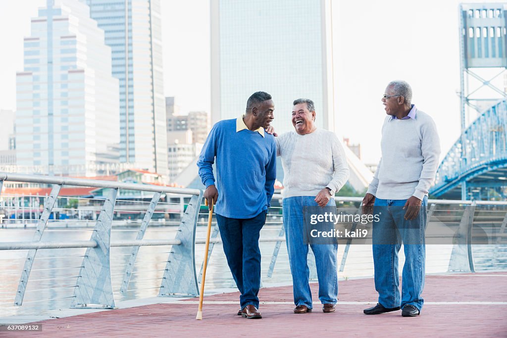 Tres hombres mayores riendo, caminando por el paseo marítimo de la ciudad