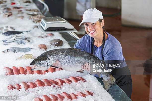 mixed race woman working in seafood market holding fish - fish vendor bildbanksfoton och bilder