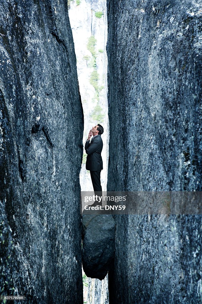 Businessman Standing On Rock Stuck In Deep Crevasse