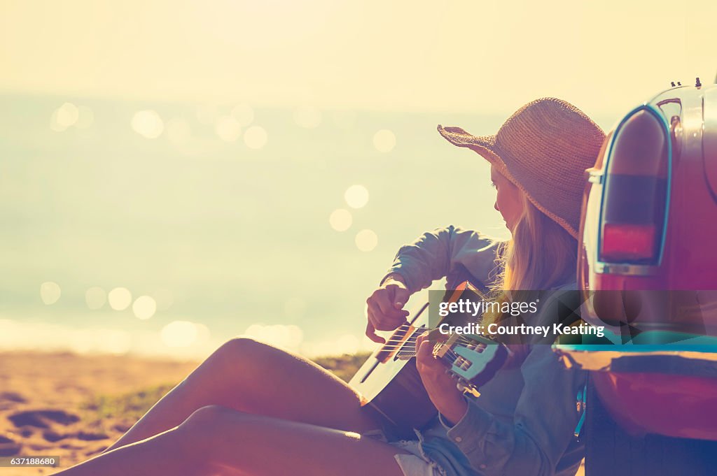 Woman with guitar leaning on a car.