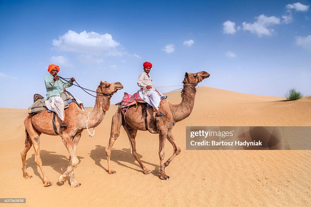 Indian men riding camels on sand dunes, Rajasthan, India