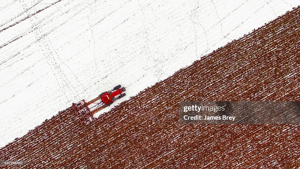 Aerial view of tractor tilling snow covered field
